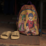 A child's backpack and sandals sit on a mat outside the shelter
