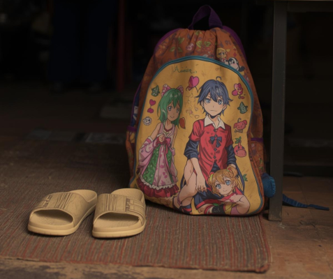 A child's backpack and sandals sit on a mat outside the shelter