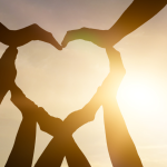 Hands forming a heart shape with sun pouring through.