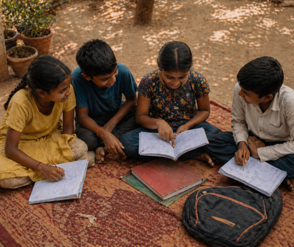 Children sitting together on a carpet in a shelter courtyard, working through homework in the afternoon