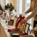 A long table of donated auction items being arranged before an event, lit by soft window light.