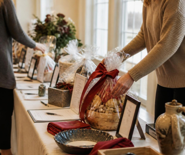 A long table of donated auction items being arranged before an event, lit by soft window light.