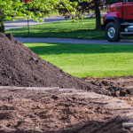 A mound of topsoil freshly delivered next to a lush lawn