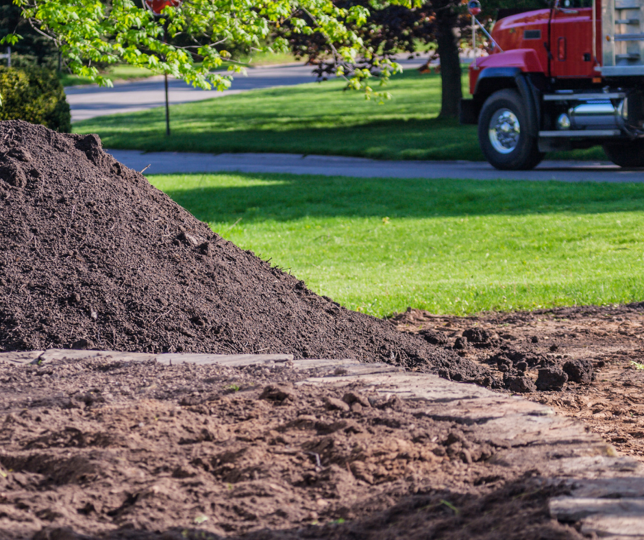 A mound of topsoil freshly delivered next to a lush lawn