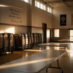 An empty community hall with stacked chairs and cleared tables in warm late-afternoon light.